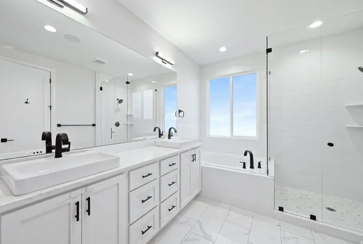 Dual vessel sinks with dark bronze fixtures, white cabinetry with dark bronze hardware, frameless glass shower enclosure, built-in soaking tub, and tile flooring
