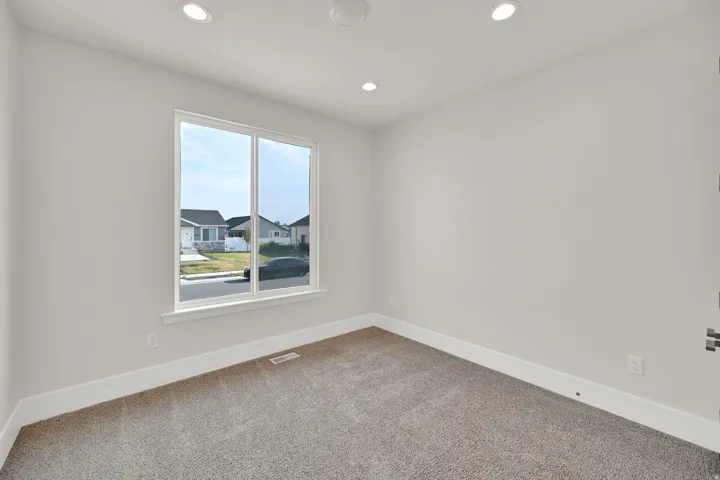 Recessed lighting, neutral wall paint, carpet flooring, and a large window with white trim