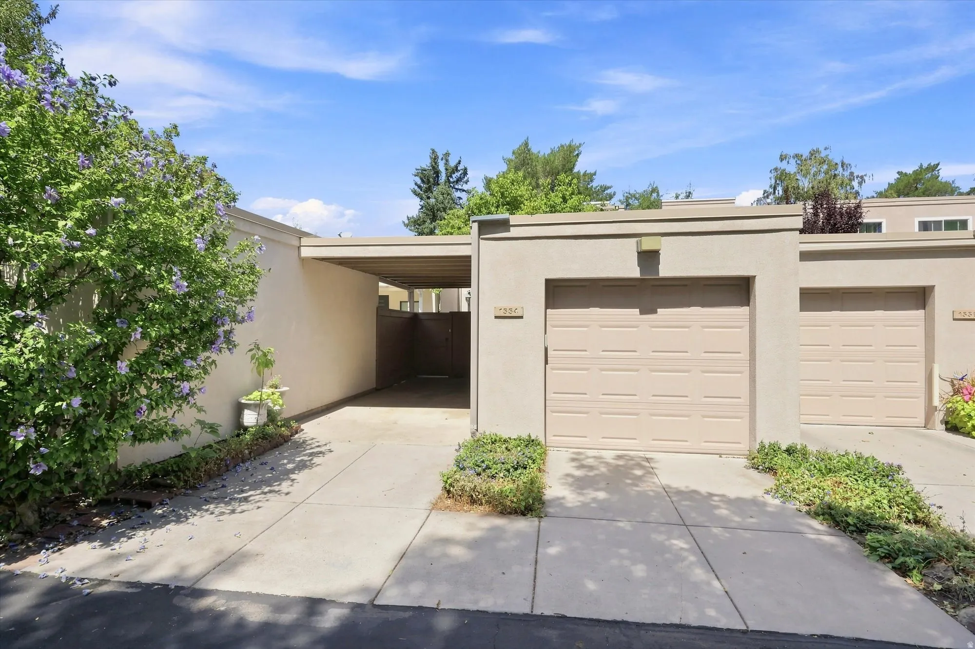 Exterior stucco finish, attached garage, covered carport, concrete driveway, and established landscaping