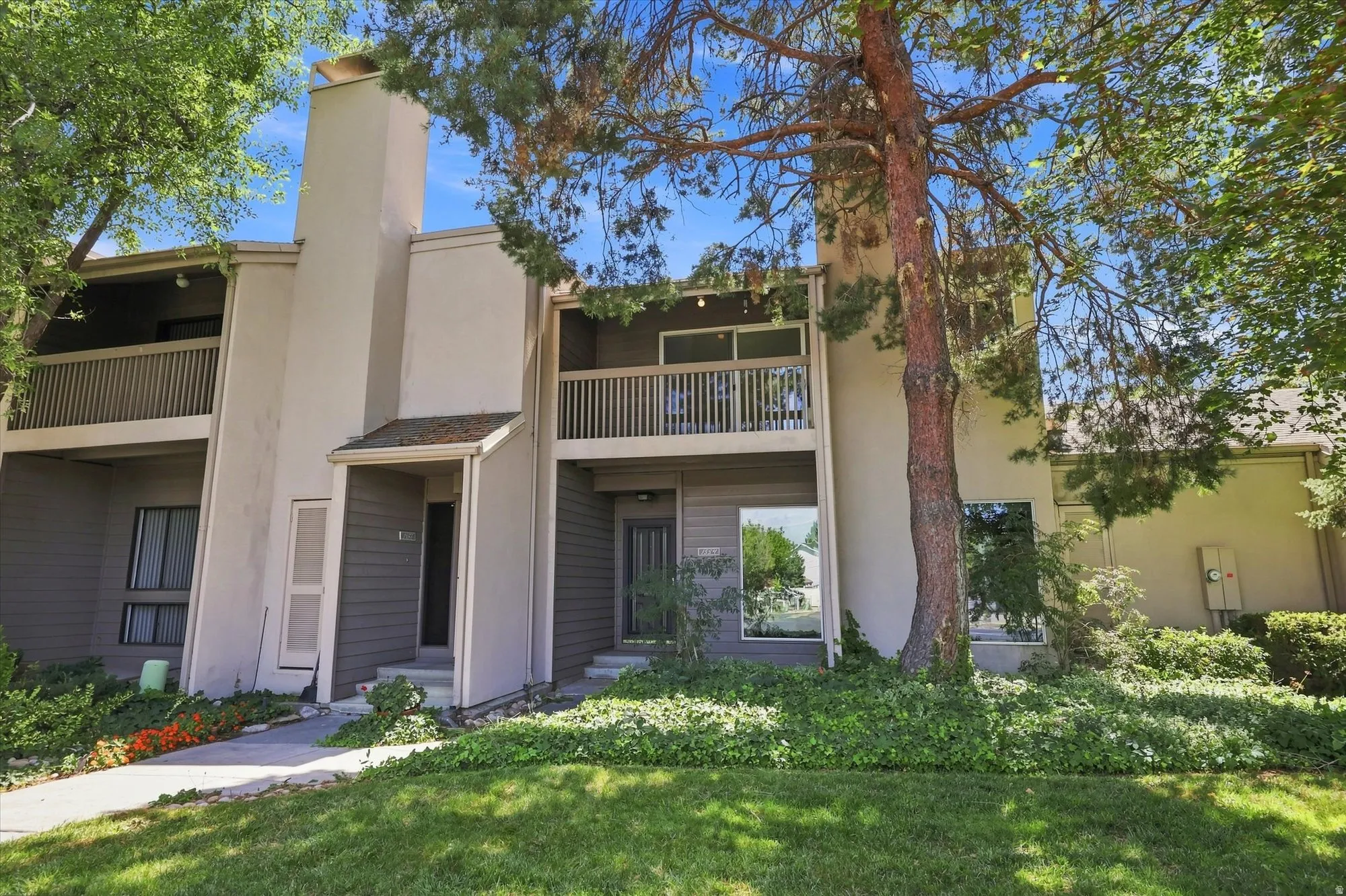 Two-story property featuring a stucco and siding exterior, multiple balconies with wood railings, a prominent chimney structure, and established landscaping