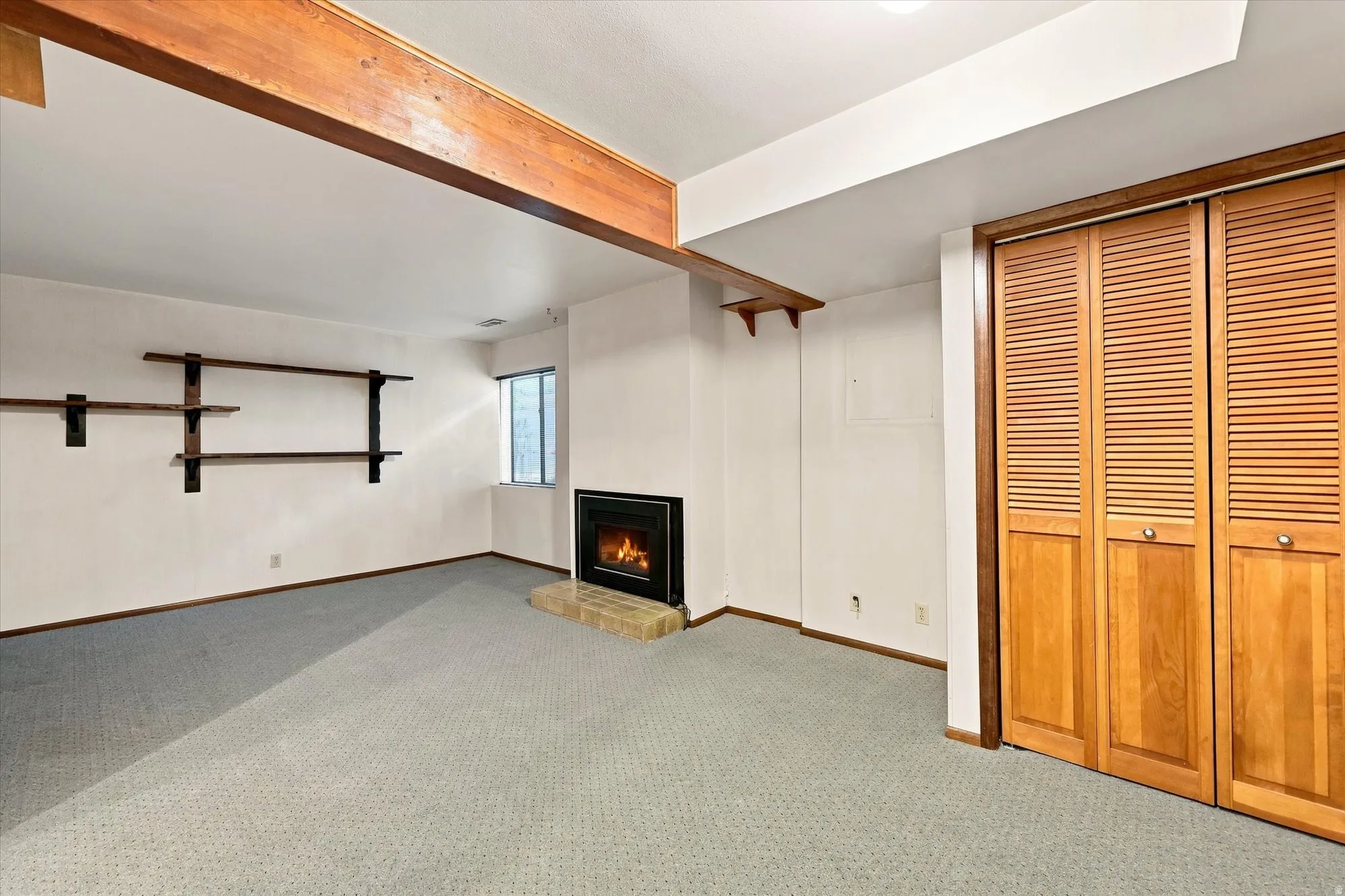 Exposed wood beam, built-in shelving, fireplace with brick hearth, double-pane window, and louvered bifold closet doors