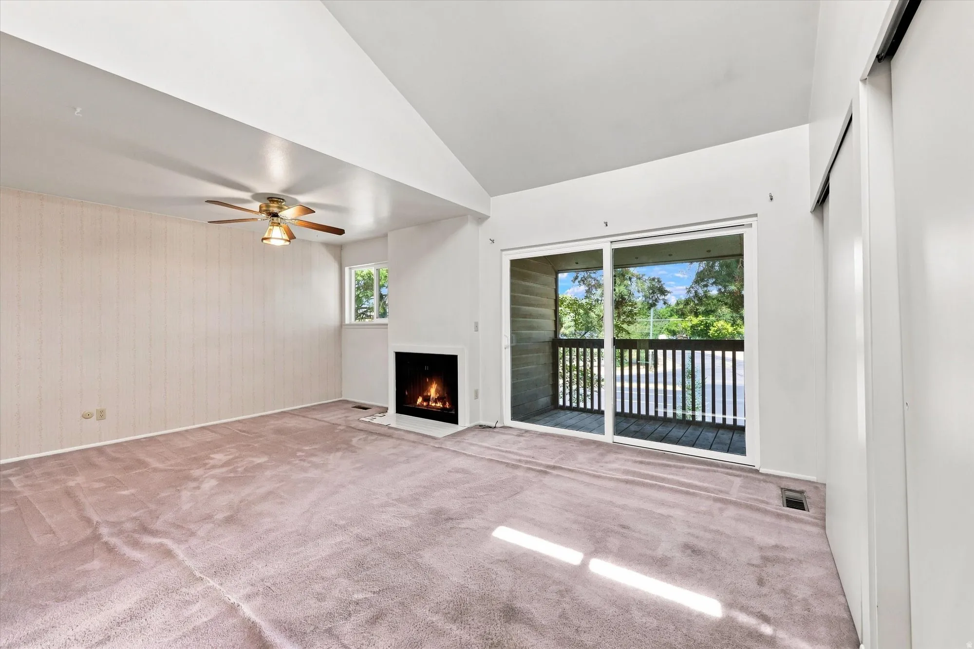 Vaulted ceiling with an attached ceiling fan, built-in fireplace, sliding glass door leading to a balcony, and a built-in closet with sliding doors