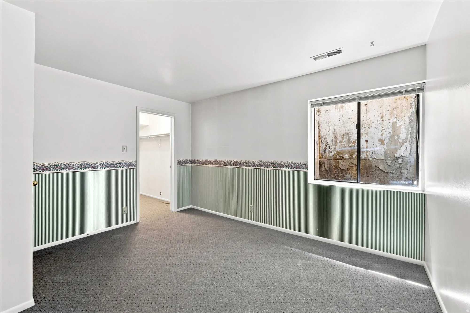 Carpeted room with a walk-in closet, a window, and painted walls with decorative trim