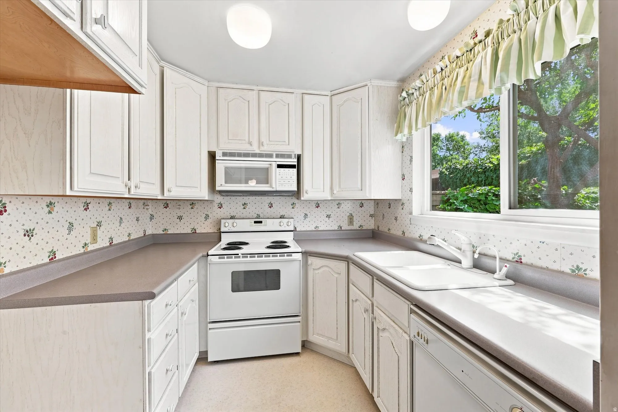 White cabinetry, a built-in microwave, an electric range, and a dishwasher, all complemented by a window over the sink