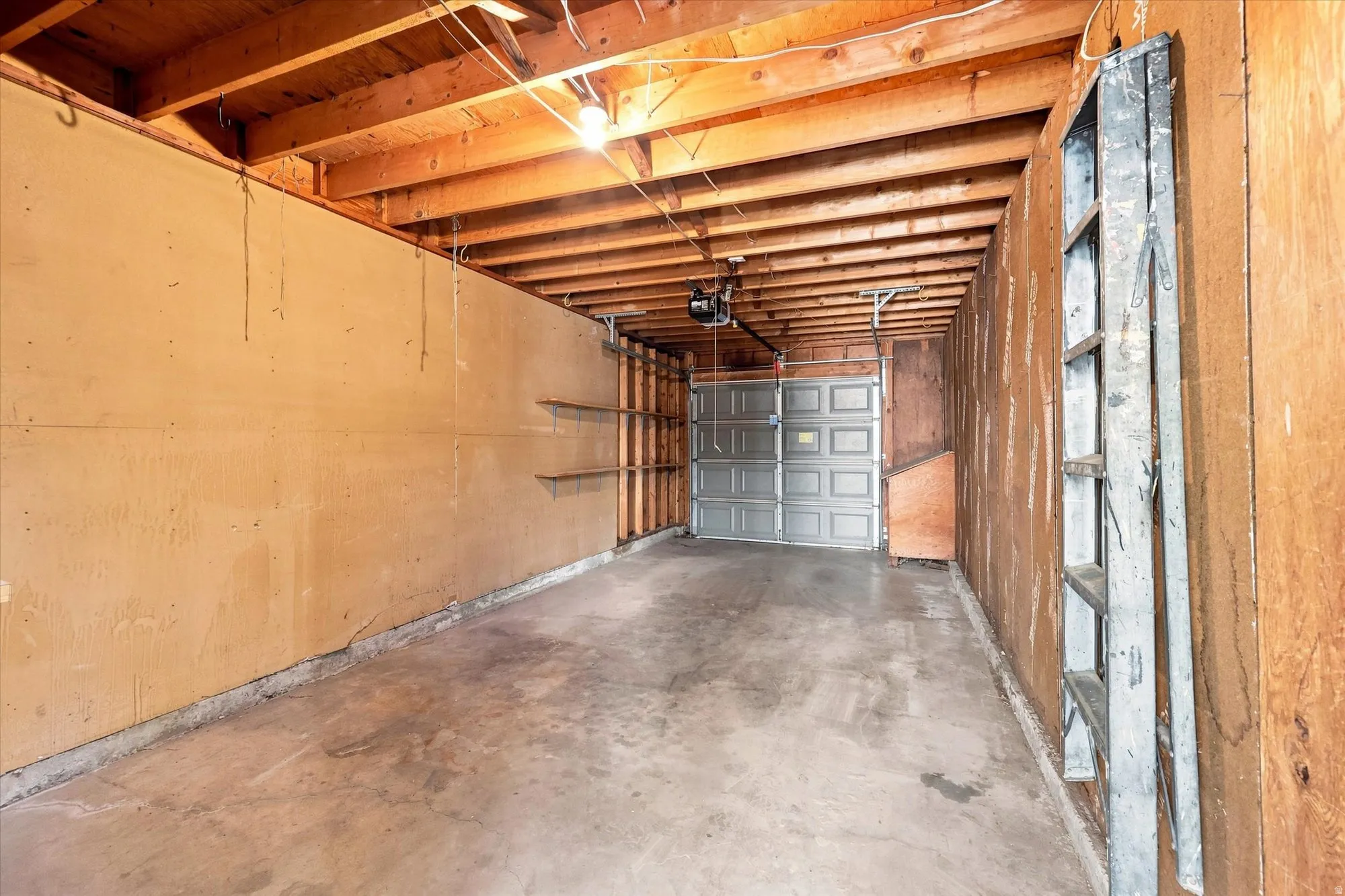 Garage space featuring an overhead door, exposed wood ceiling joists, and concrete flooring