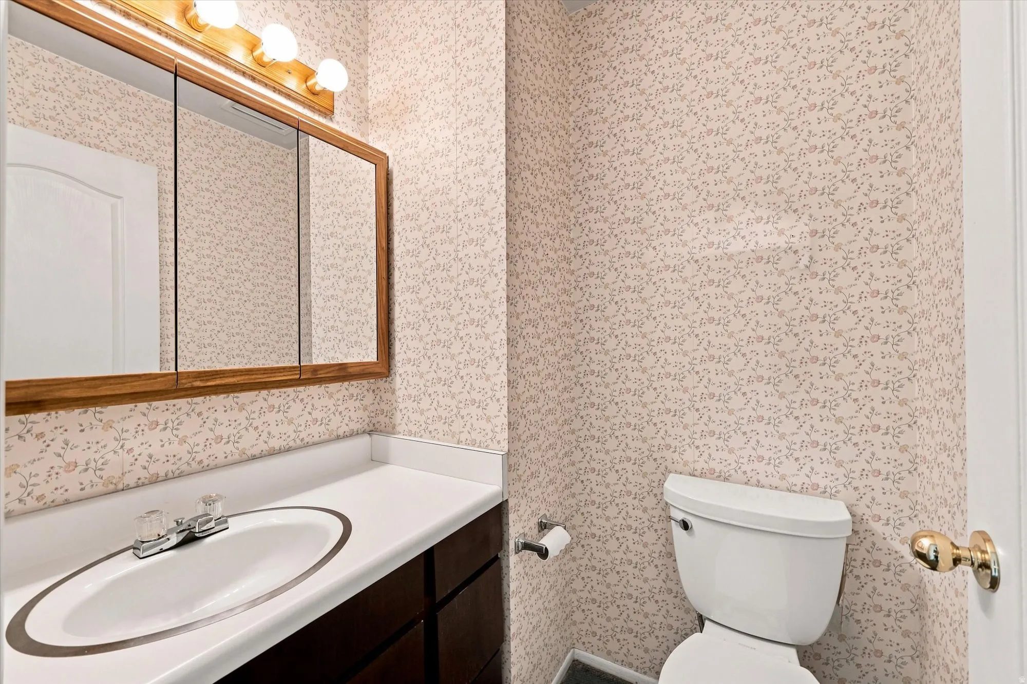 Vanity with integrated sink, chrome faucet, wood-framed medicine cabinet, and three-bulb vanity light fixture