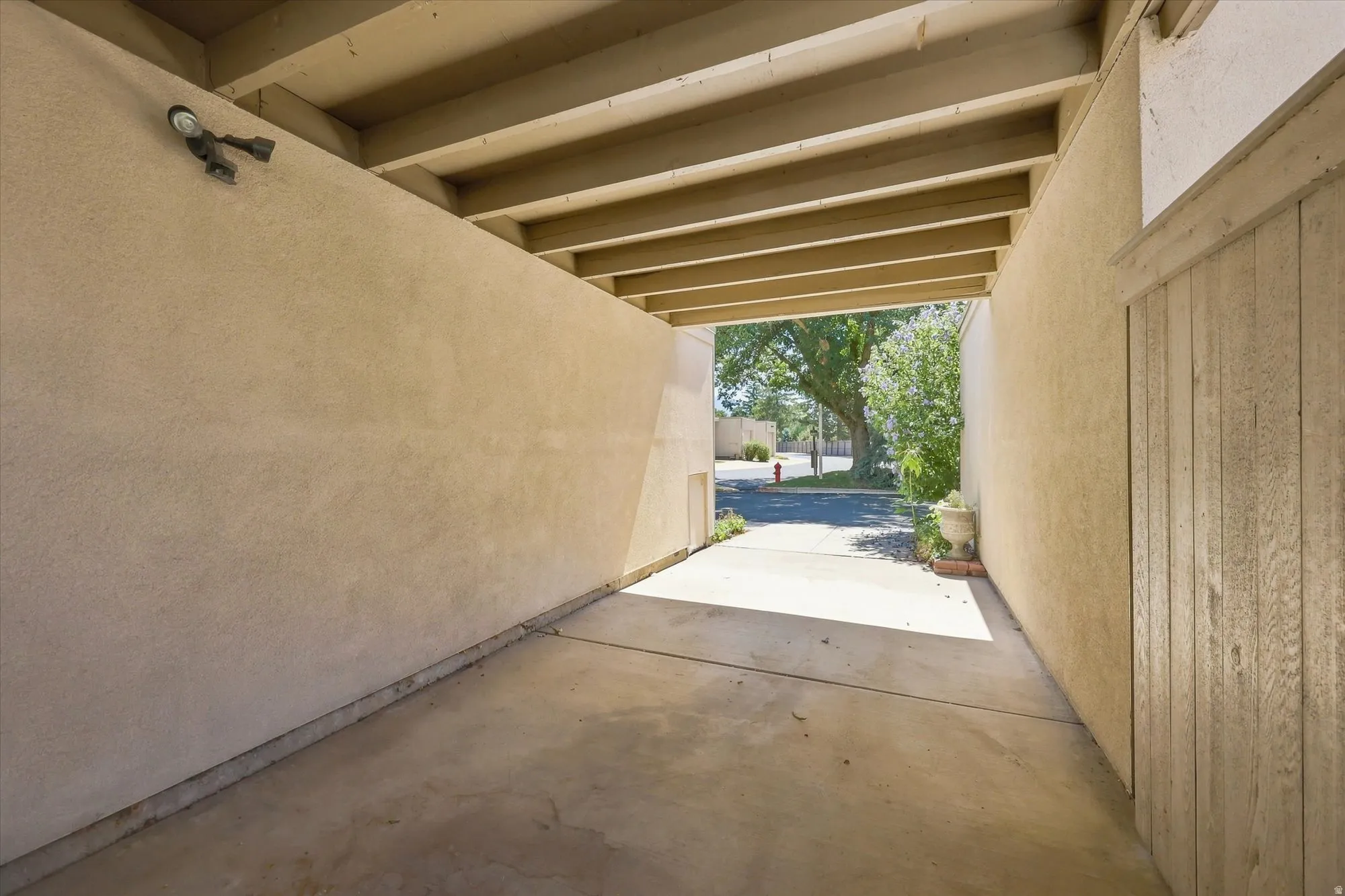 Covered carport featuring an exposed beam ceiling, stucco walls, and a concrete floor
