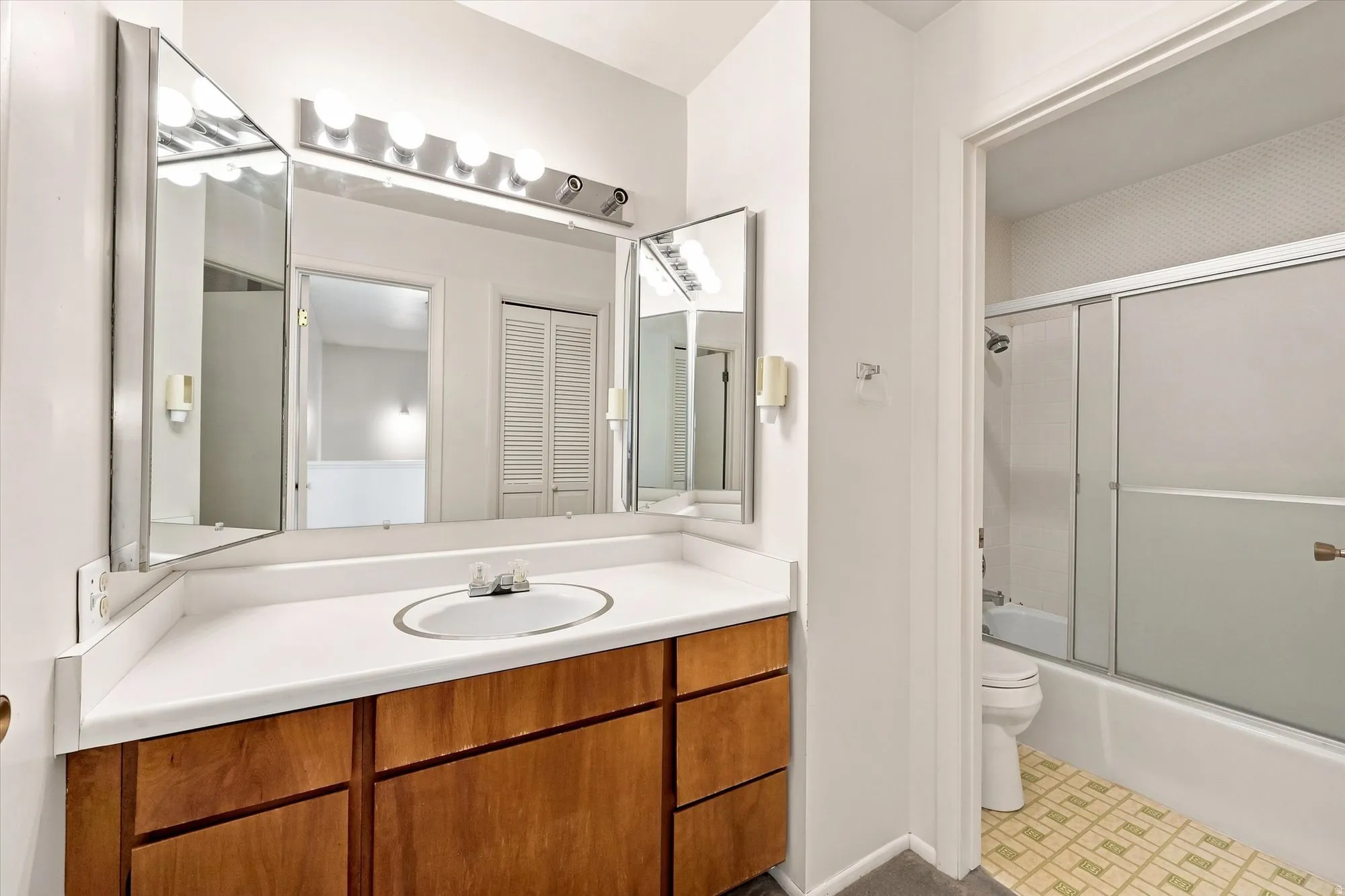 Vanity with wood-finish cabinetry and a white countertop, featuring an integrated sink, three-panel mirrored medicine cabinet, and a vanity light bar
