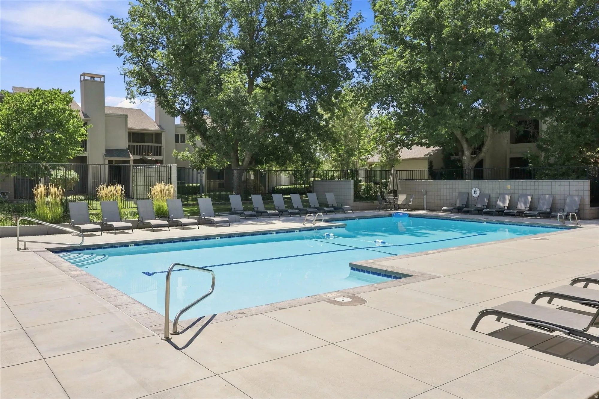Rectangular swimming pool with integrated steps, surrounded by a concrete pool deck, and perimeter fencing