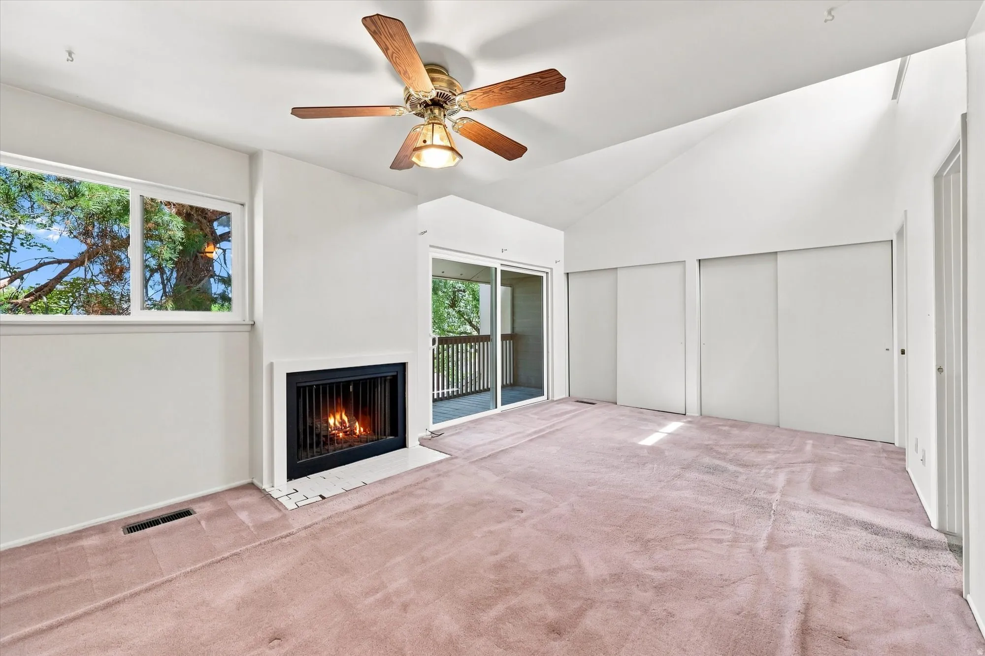Vaulted ceiling featuring a ceiling fan, fireplace with a white hearth, sliding glass door, and multiple windows