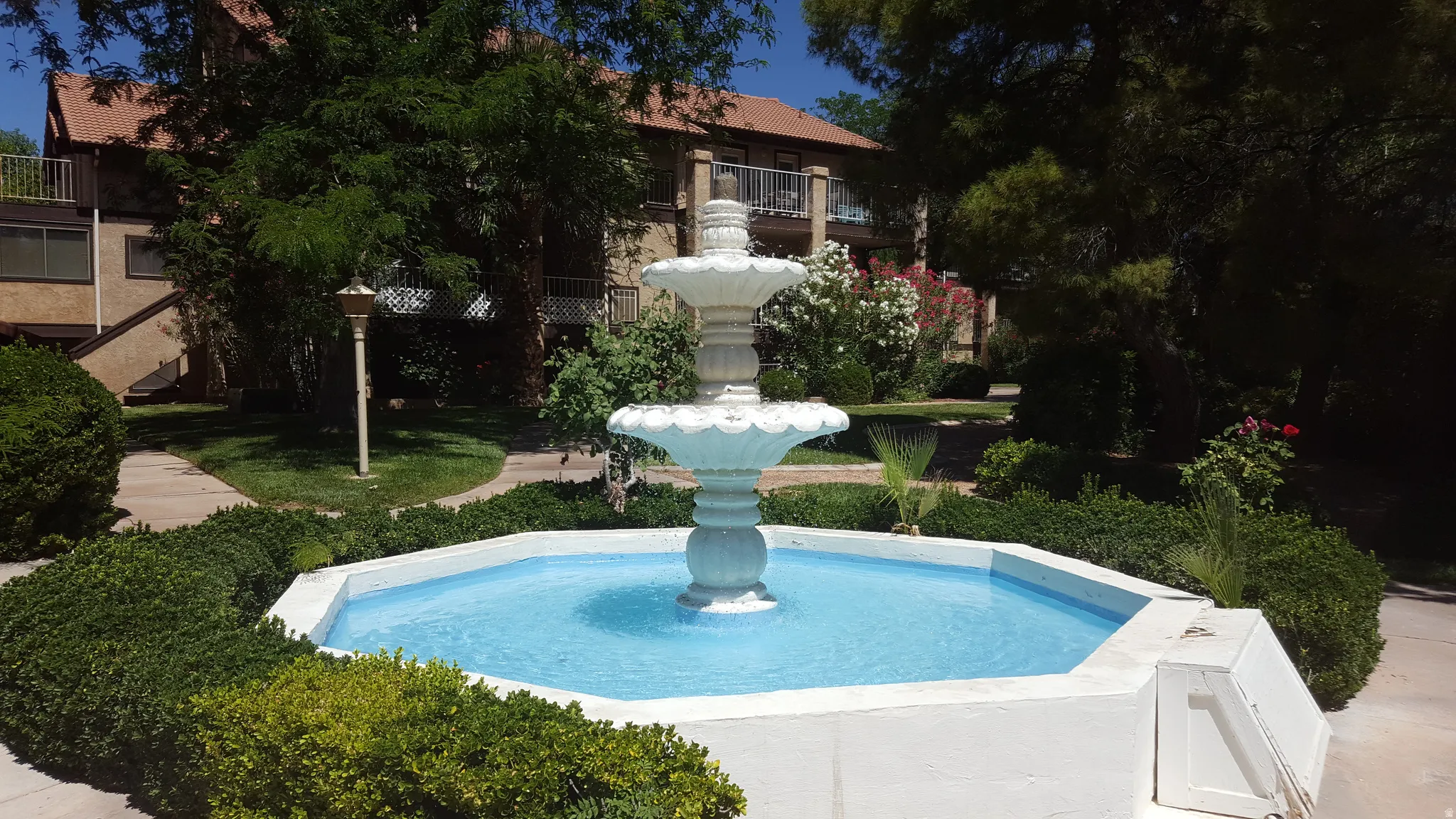 Tiered outdoor fountain with surrounding landscaped greenery and paved walkways