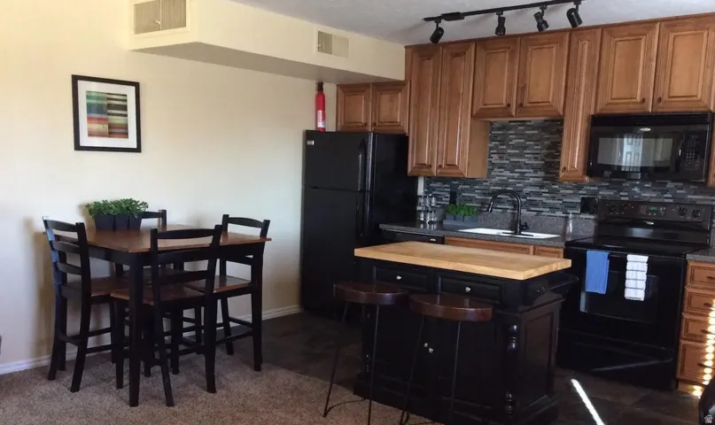 Kitchen featuring wood-finish cabinetry, black appliances, a mosaic tile backsplash, and a portable island with a wood countertop