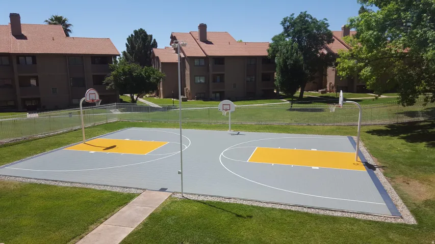 Recreational basketball court with two hoops, surrounded by a chain-link fence and green lawn