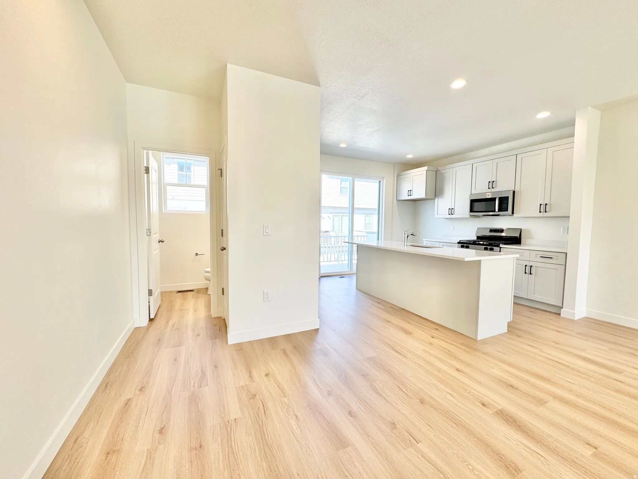Wood-finish flooring throughout, kitchen with white shaker cabinetry, stainless steel appliances, central island, and recessed lighting