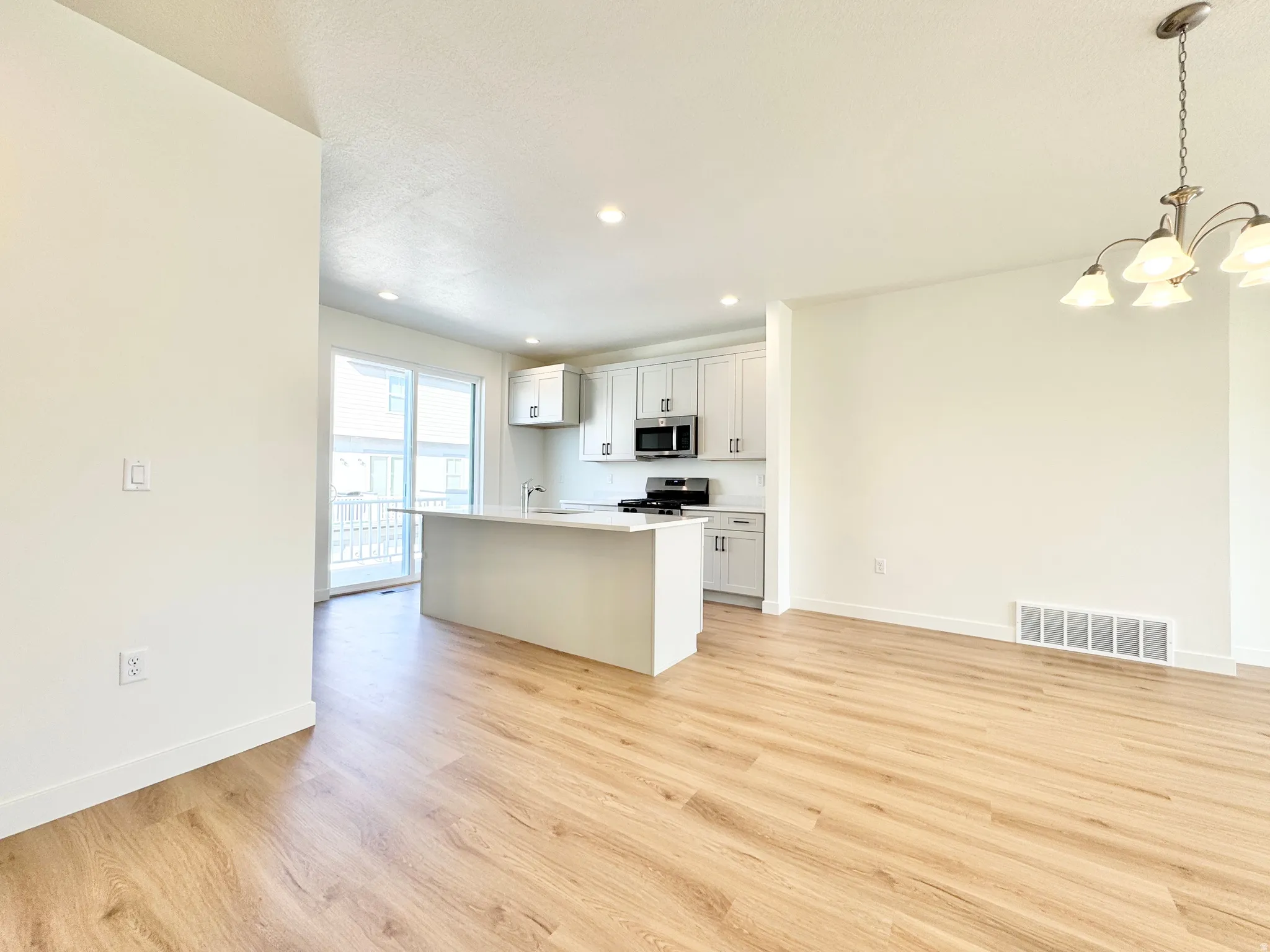 Open-concept living area featuring wood-finish flooring, recessed lighting, and a modern kitchen island with white cabinetry