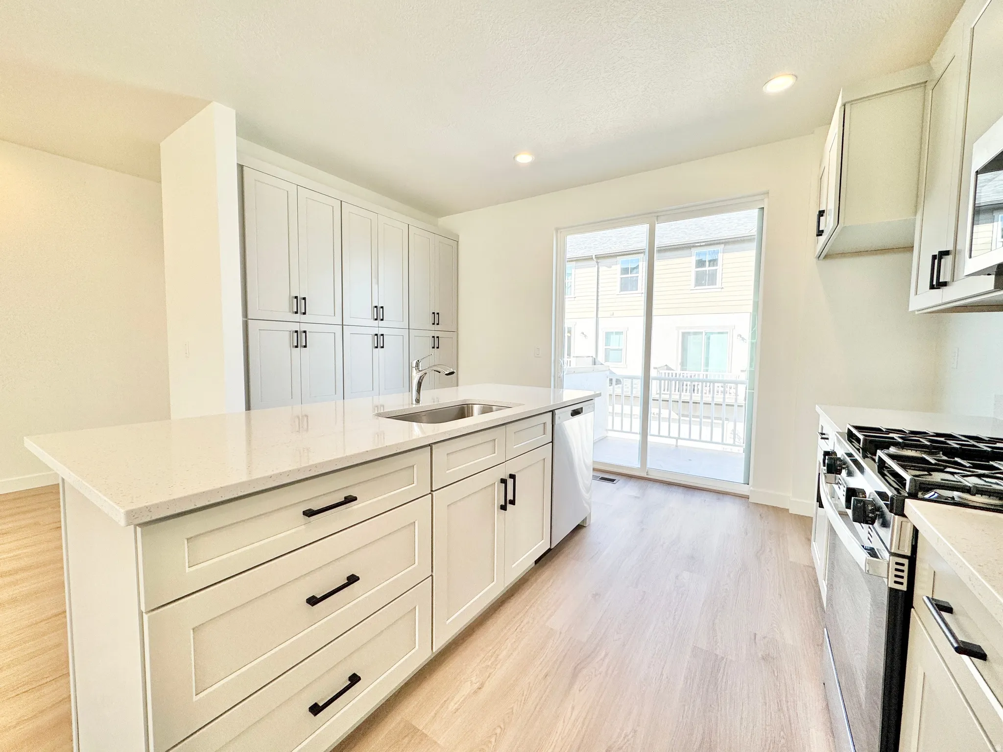 Kitchen featuring light wood-finish flooring, white shaker cabinetry with matte black hardware, light-toned countertop, stainless steel appliances, and a sliding glass door
