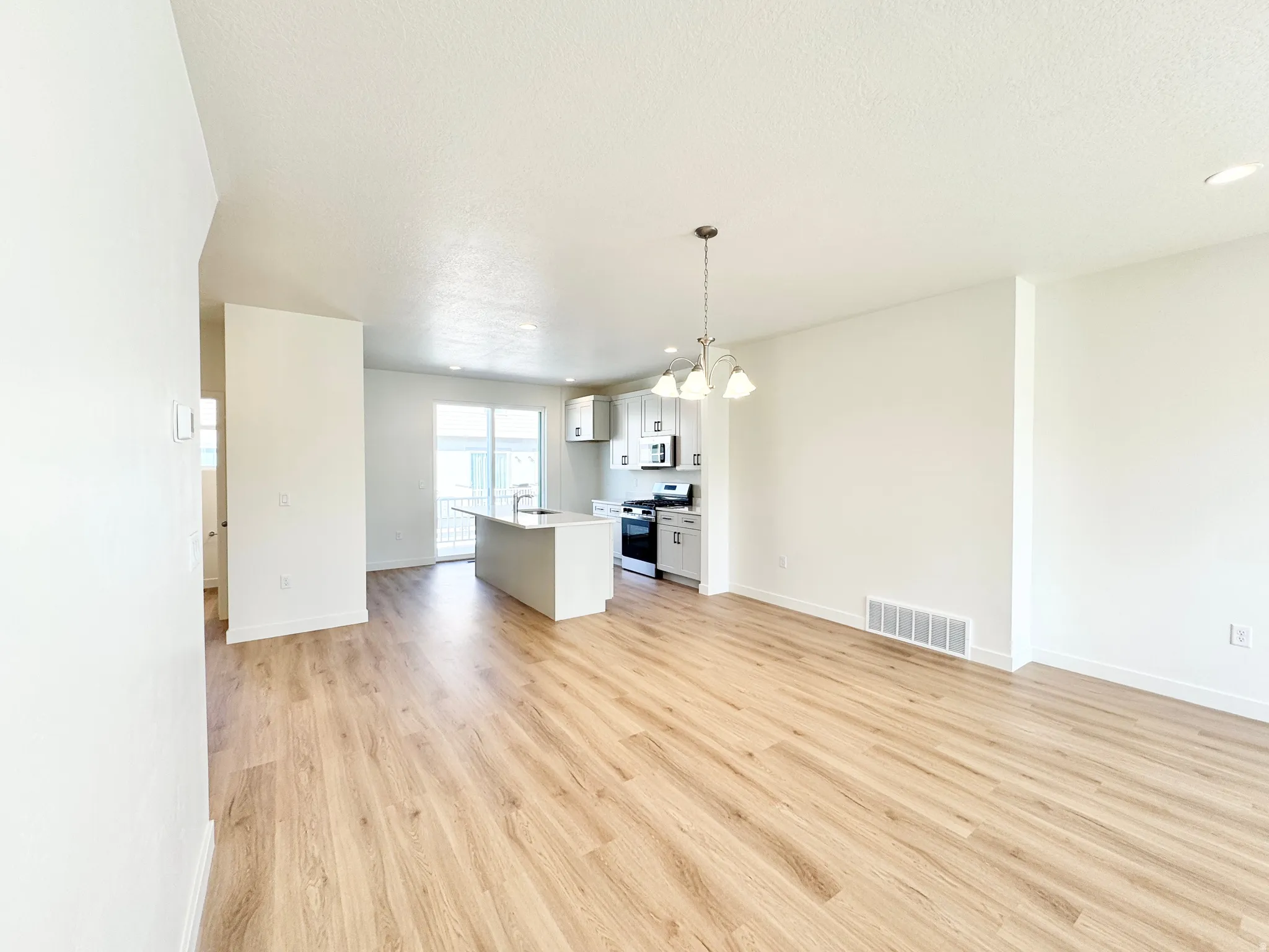Open-concept main level featuring wood-finish flooring, a kitchen island with seating, pendant lighting, and stainless steel appliances