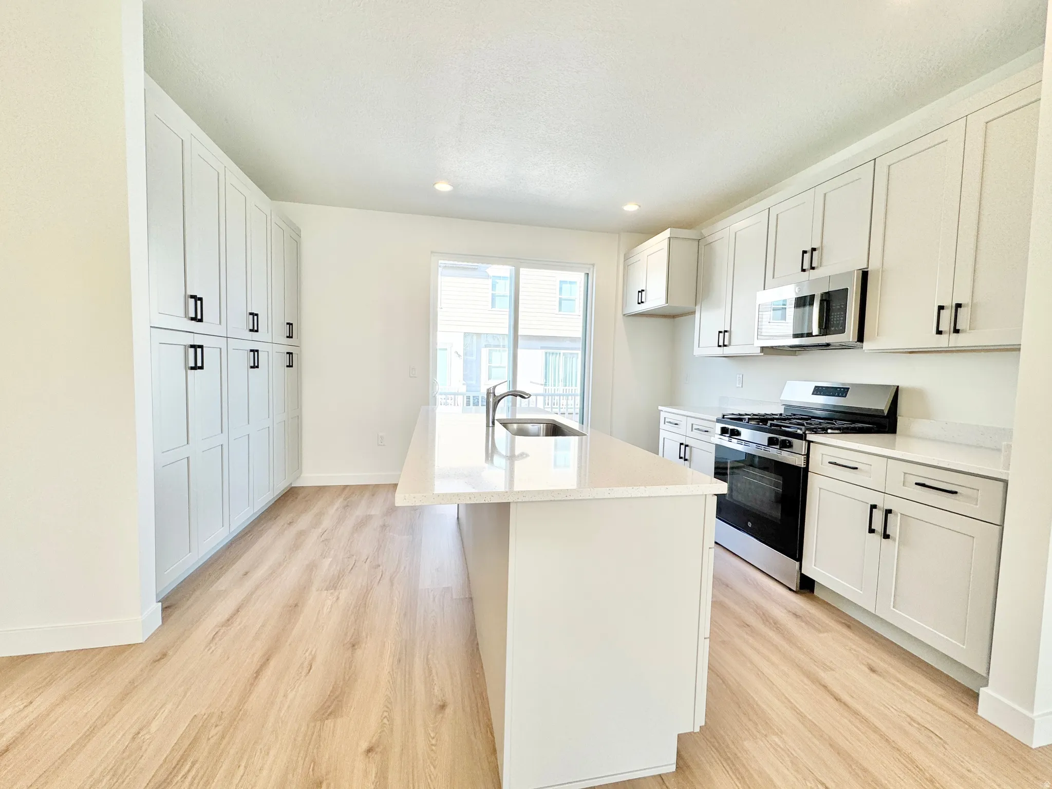 White shaker cabinetry, stainless steel appliances, wood-finish flooring, recessed lighting, and a kitchen island with an undermount sink
