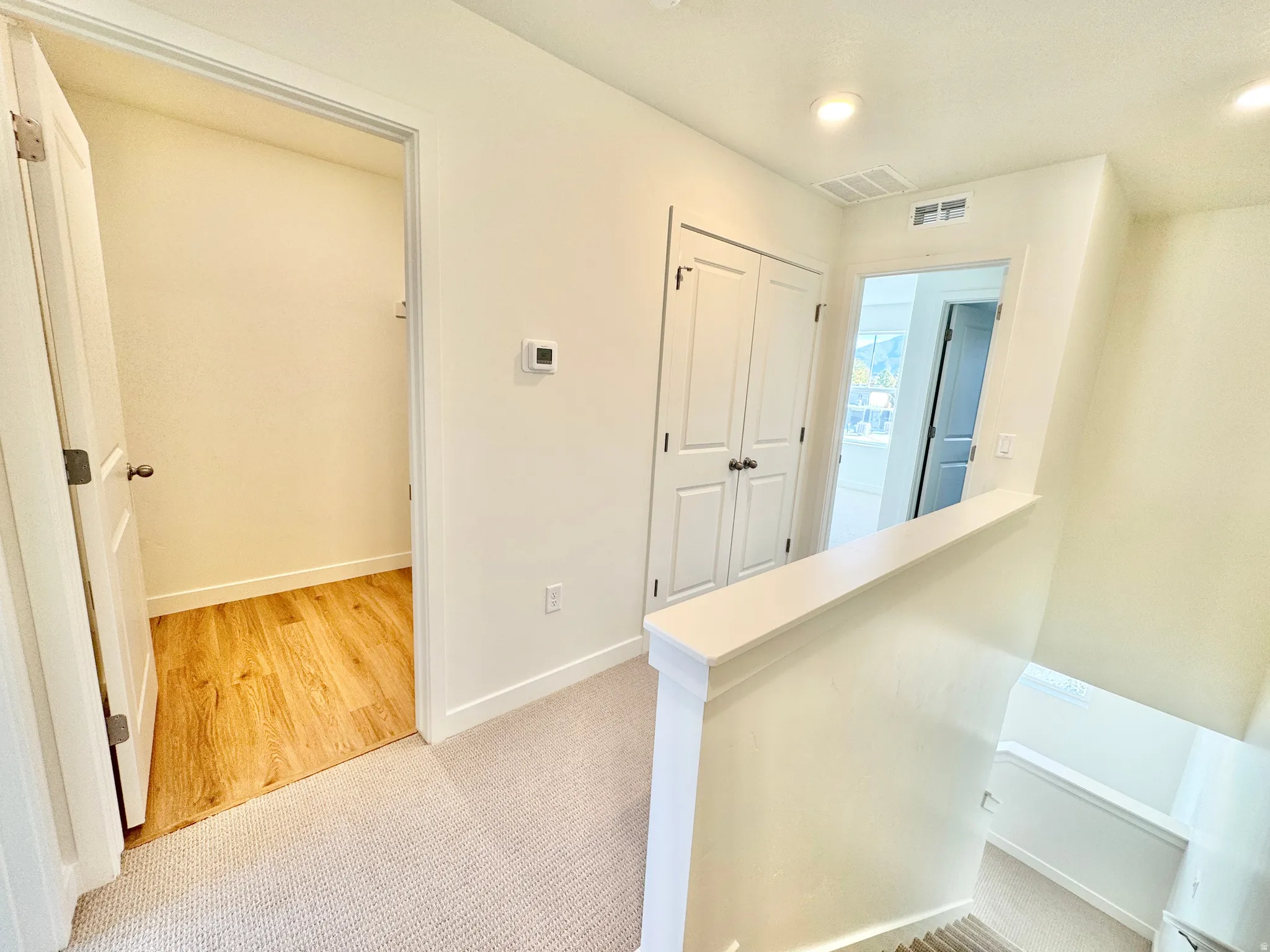 Recessed lighting illuminates the upper hall with light-toned carpeting, a built-in closet, and a half-wall overlooking the stairwell