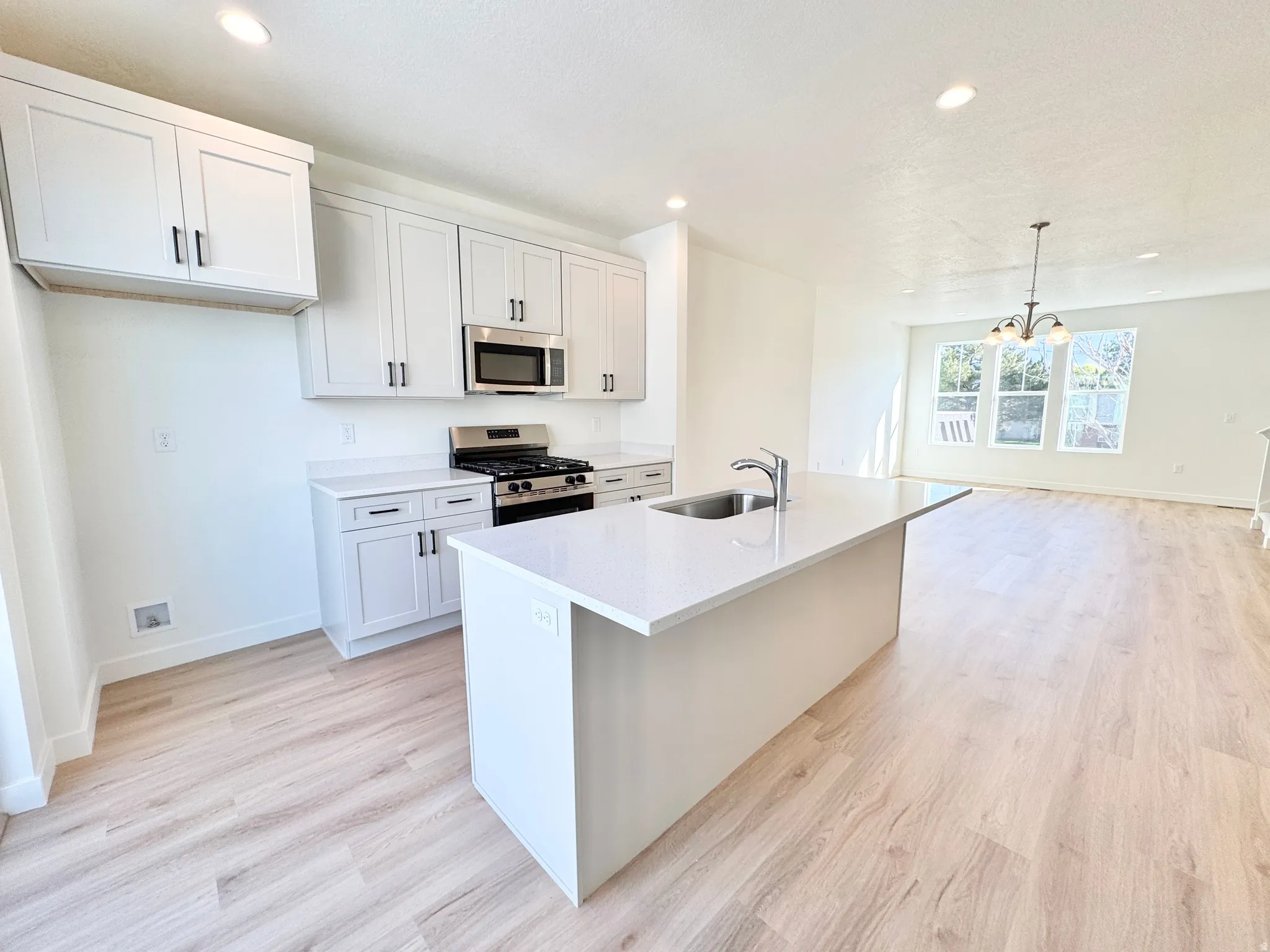 Kitchen featuring light-finish flooring, white cabinetry with dark hardware, a center island with an integrated sink, stainless steel appliances, and recessed lighting
