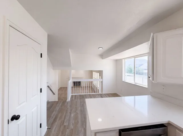 White paneled door with black hardware, wood-finish flooring, white baluster railing, white cabinetry, and white countertop