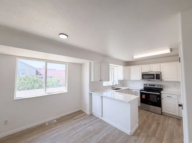 Kitchen featuring a U-shaped layout, white cabinetry, integrated stainless steel appliances, white countertops, and wood-finish flooring
