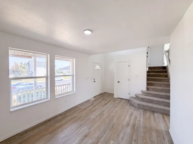 Bright, open living space featuring expansive windows with natural light, wood-finish flooring throughout, and a staircase with wood treads