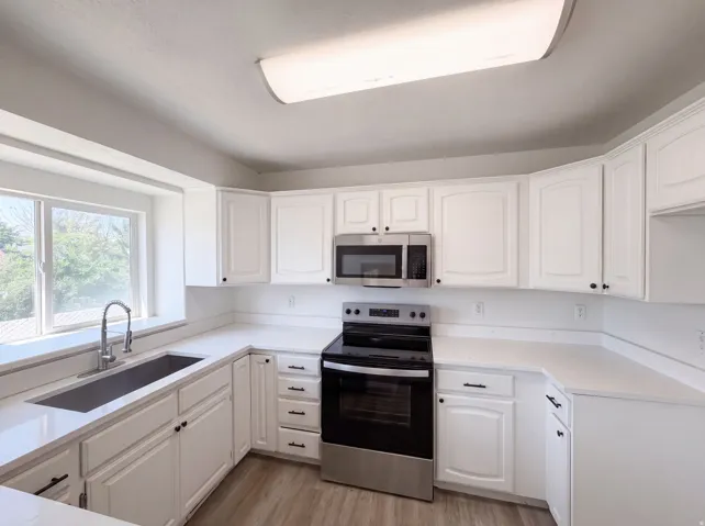 Bright, updated kitchen featuring crisp white cabinetry with black hardware, stainless steel appliances including a gas range and over-the-range microwave, white quartz countertops, an undermount sink with pull-down faucet, recessed ceiling lighting, and