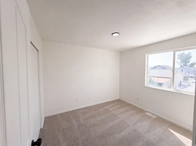 Bright secondary bedroom featuring neutral wall finishes, carpet flooring, and dual windows with natural light exposure