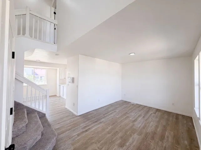 Spacious bedroom with wood-finish flooring, abundant natural light from dual windows, and clean white walls