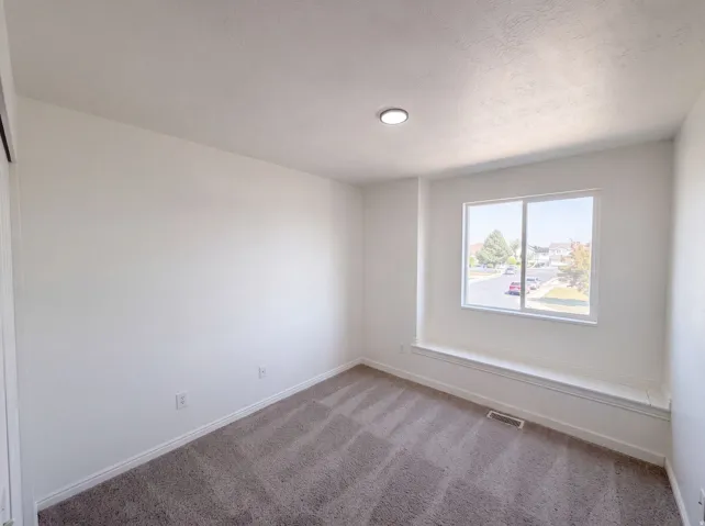 Bright secondary bedroom with large double-hung window, neutral wall finishes, and plush carpeting throughout