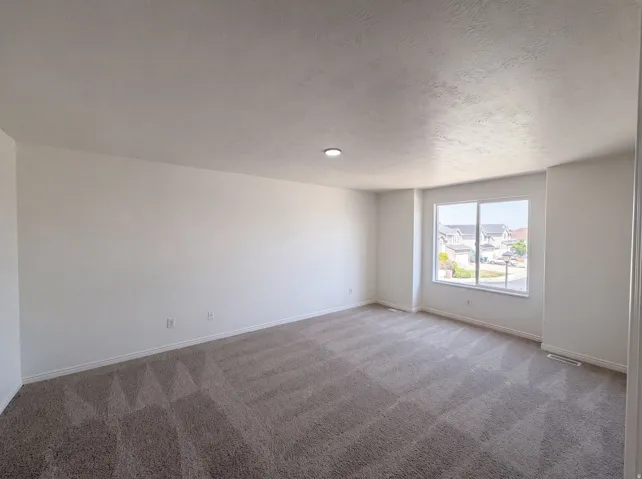 Spacious room featuring neutral carpeting, white walls, and a large window