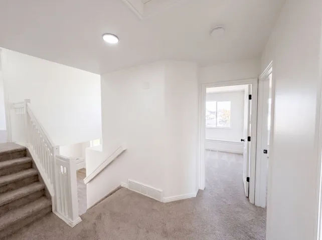 Bright upper-level landing featuring neutral carpeting, recessed lighting, and white painted walls with clean architectural lines