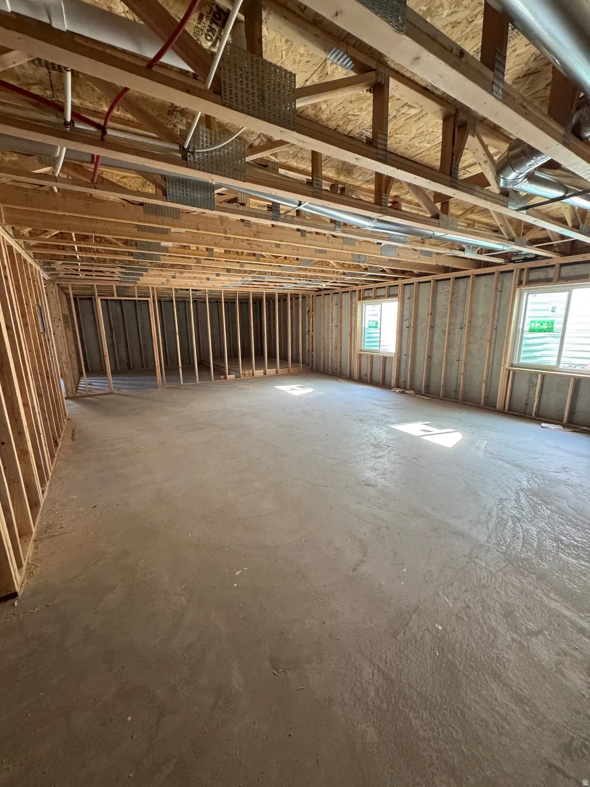 Spacious open interior with concrete flooring, exposed wood beam ceiling structure, and metal stud framing throughout