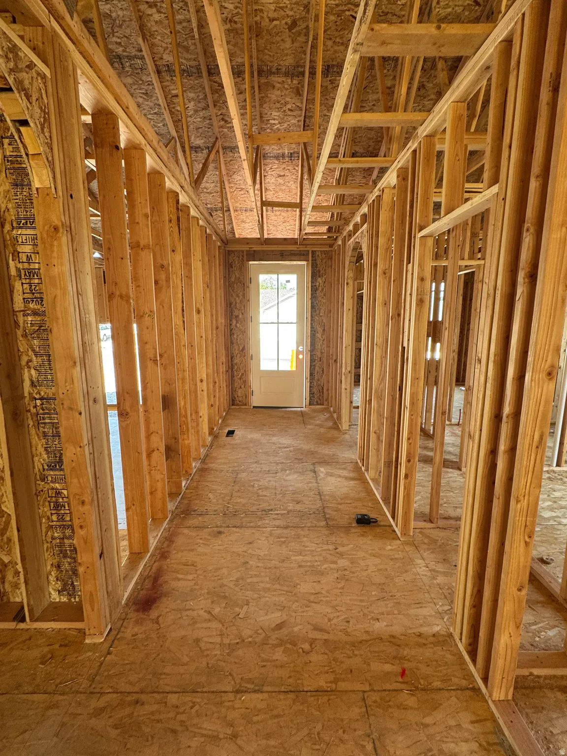 Hallway featuring wood-framed stud construction with exposed insulation, wood-finish subflooring, and recessed ceiling joists