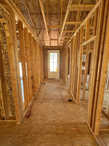 Hallway featuring wood-framed stud construction with exposed insulation, wood-finish subflooring, and recessed ceiling joists