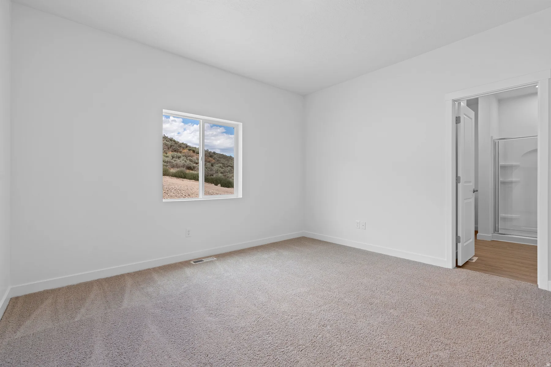 Bright and spacious bedroom with neutral wall finishes, carpeted flooring, and abundant natural light from a large window