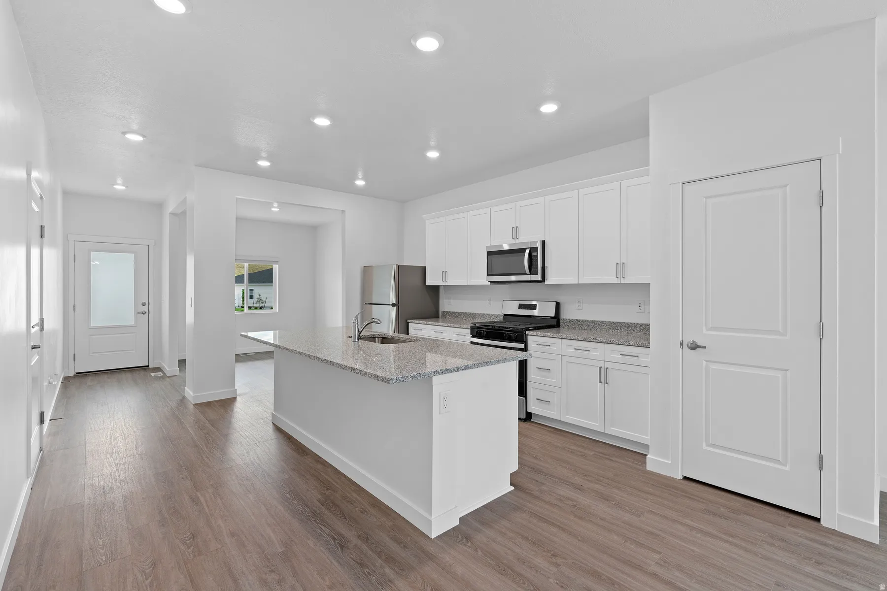 Kitchen featuring a center island with sink, stainless steel appliances, white cabinetry, and granite countertops