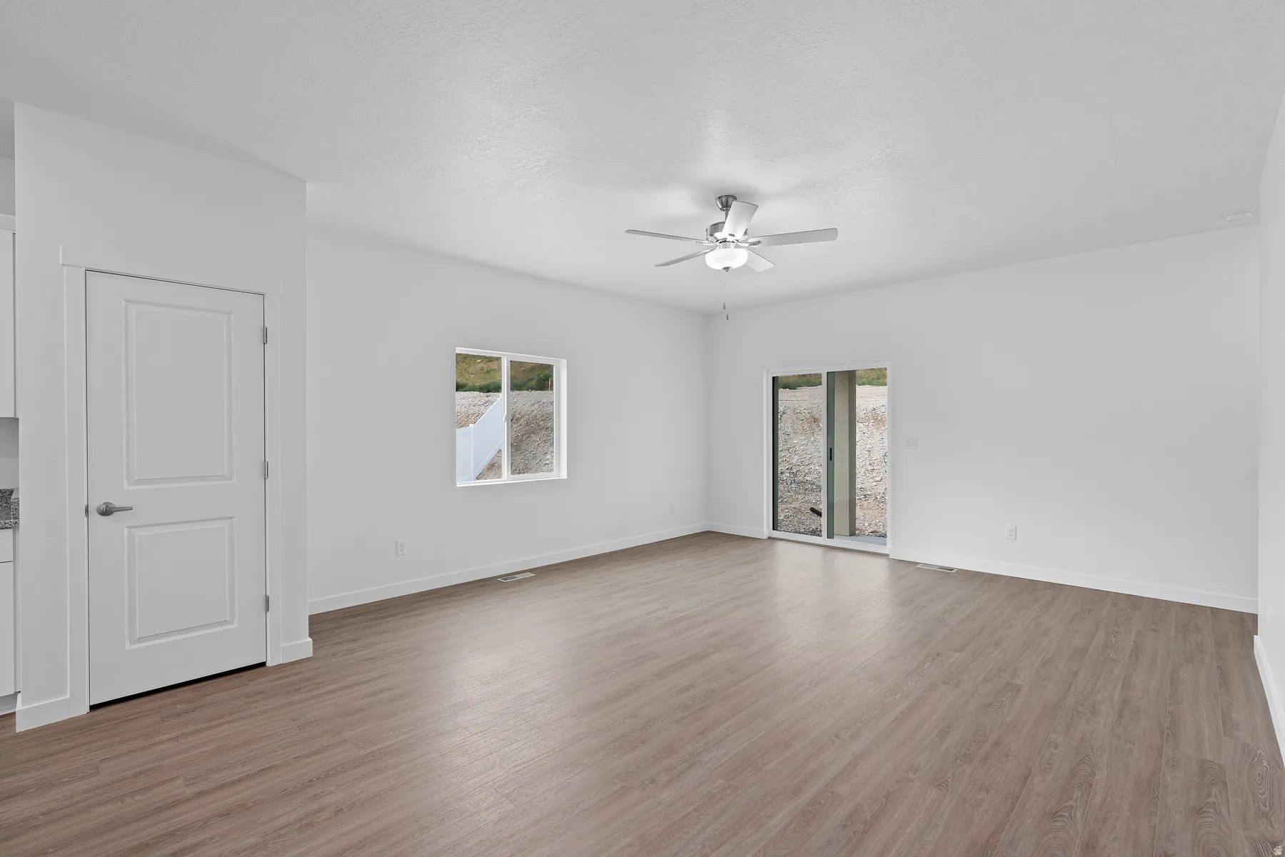 Spacious room featuring wood-finish flooring, a contemporary ceiling fan, and white walls
