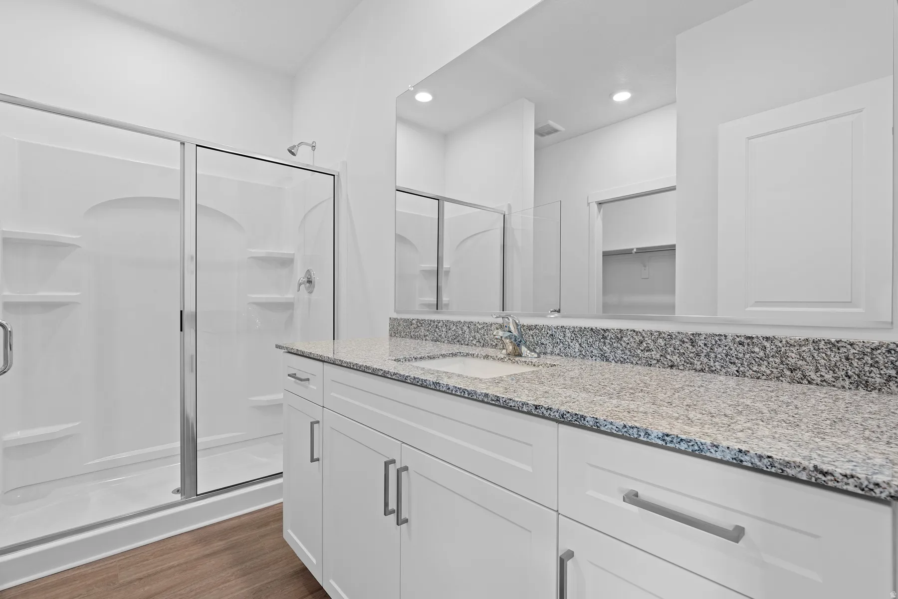 White shaker-style cabinetry with chrome hardware, speckled countertop, and wood-finish flooring