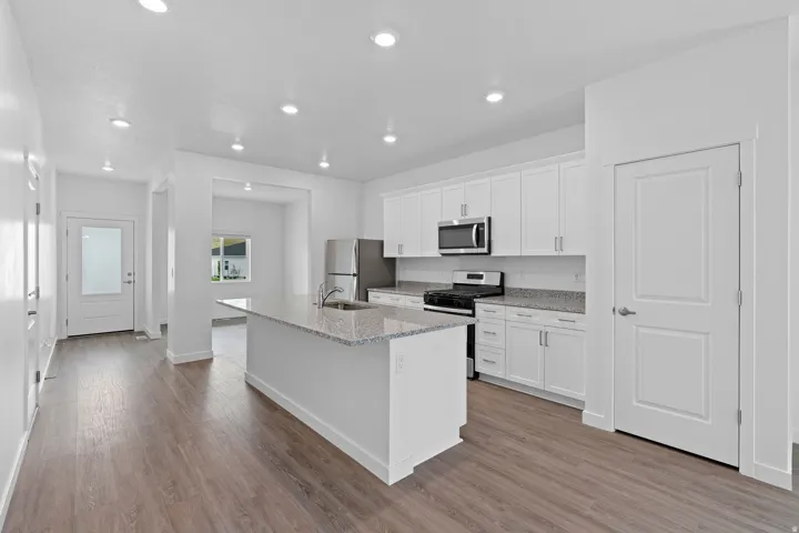 Kitchen featuring a center island with sink, stainless steel appliances, white cabinetry, and granite countertops