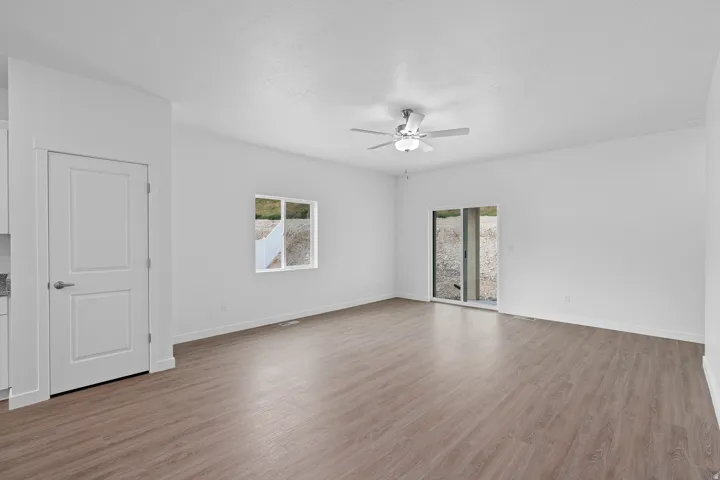 Spacious room featuring wood-finish flooring, a contemporary ceiling fan, and white walls