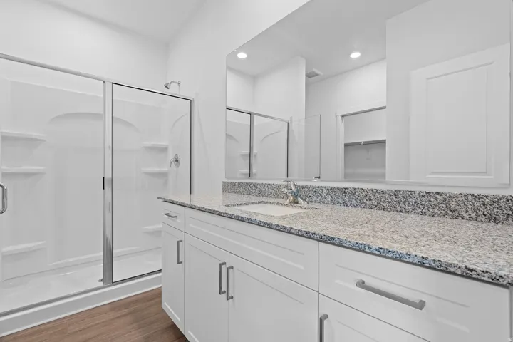 White shaker-style cabinetry with chrome hardware, speckled countertop, and wood-finish flooring