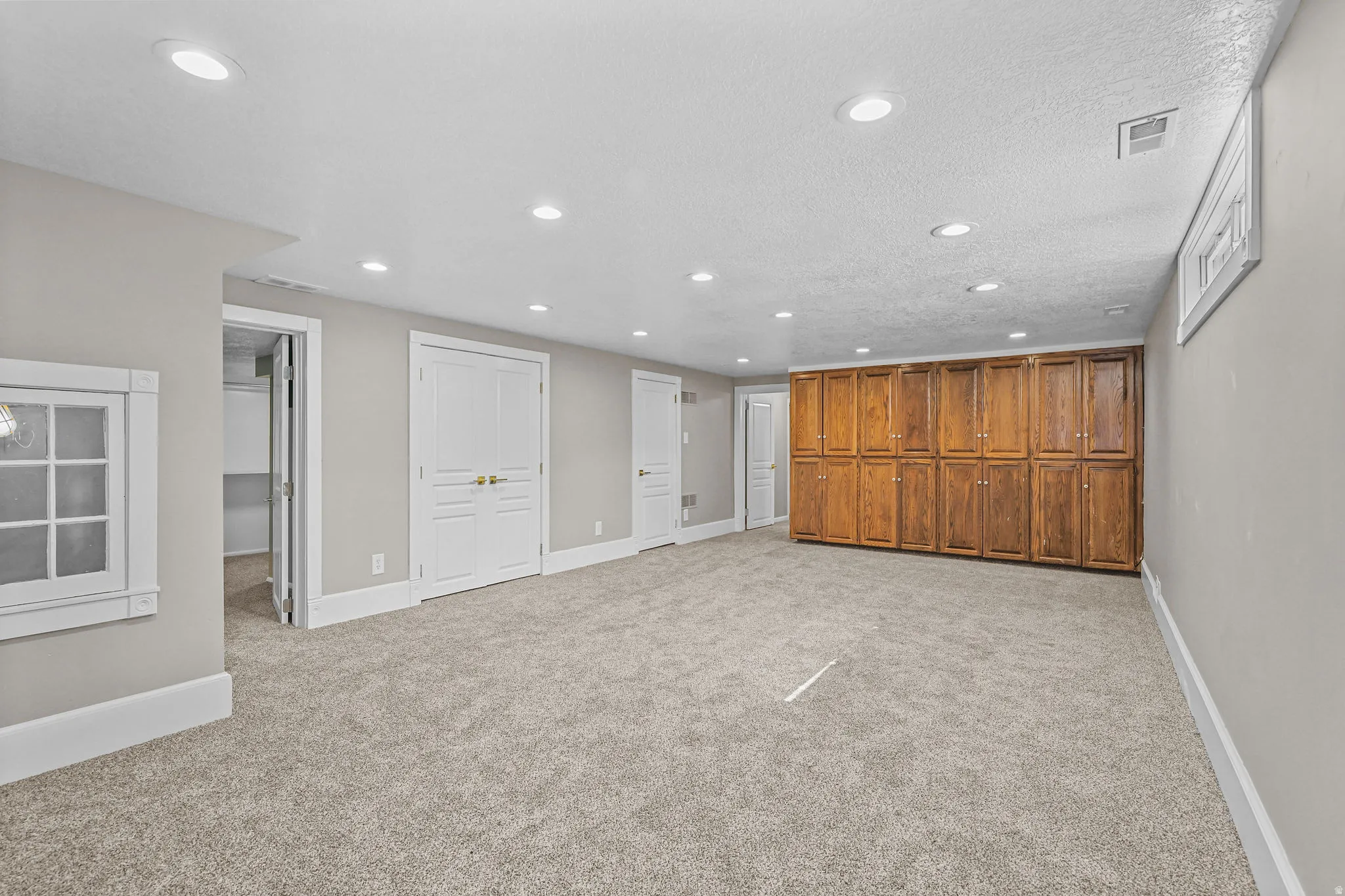 Recessed lighting, plush carpet flooring, wood-finish cabinetry, white trim, and a window well