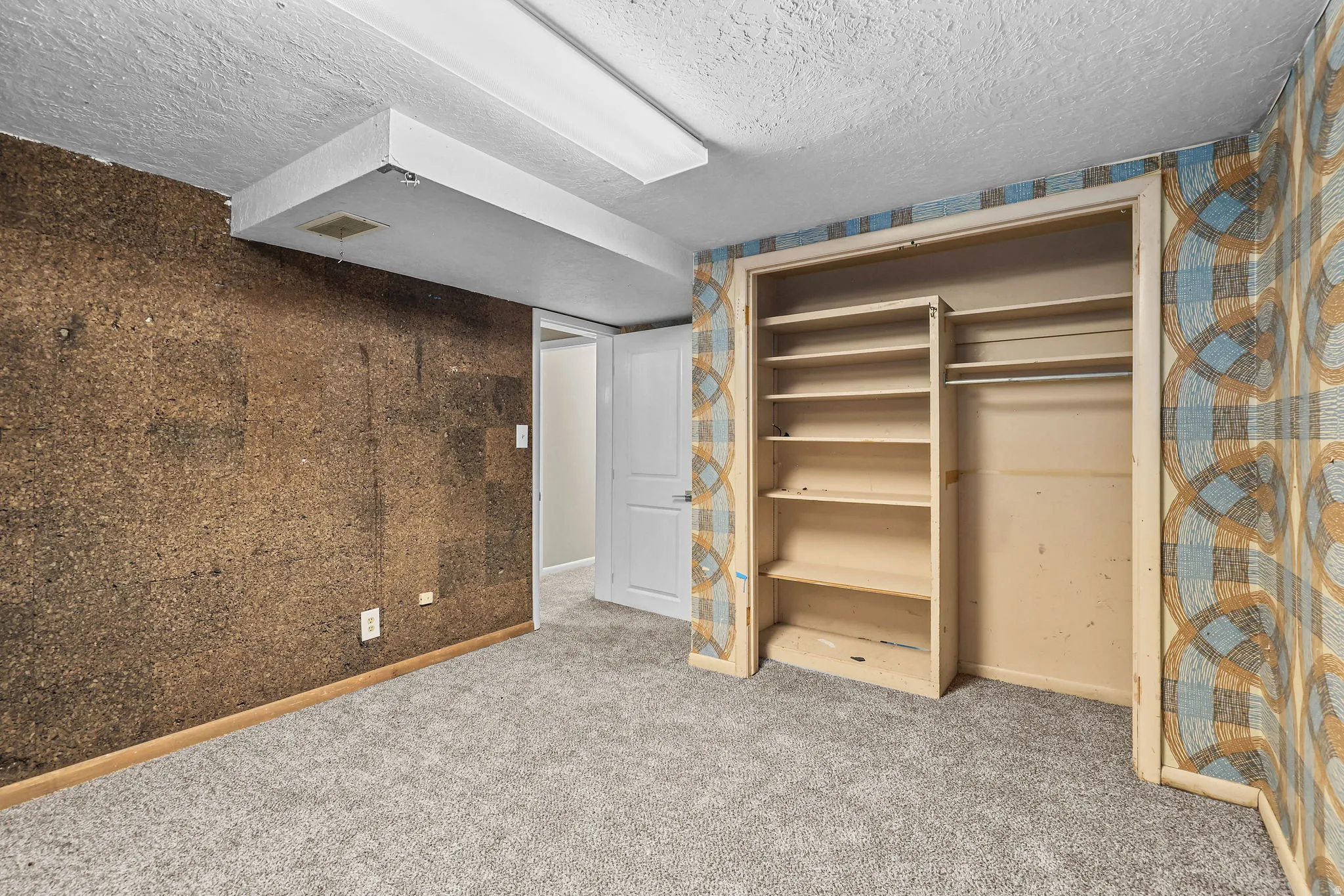 Wall-to-wall carpeting with built-in shelving, a clothing rod, and a partial cork wall covering