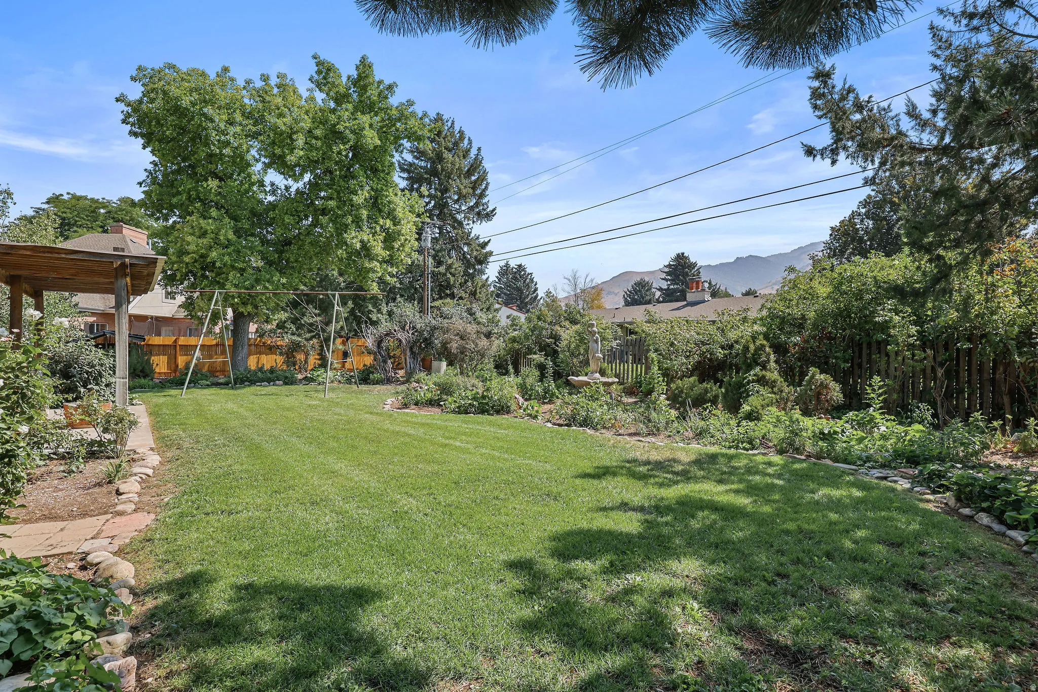 Expansive yard featuring a manicured lawn, established landscaping, and a wooden pergola