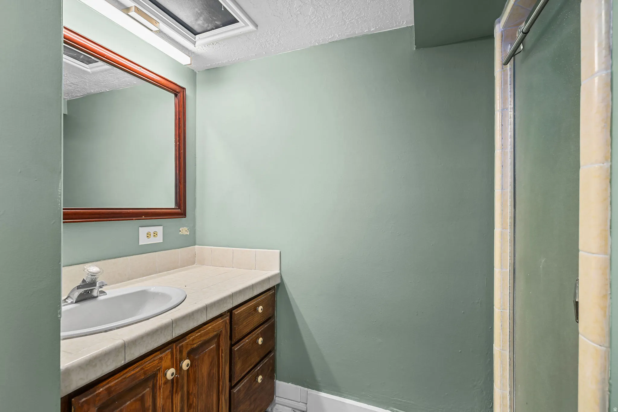 Wood-finish vanity cabinetry with a tiled countertop, undermount sink, and framed wall mirror