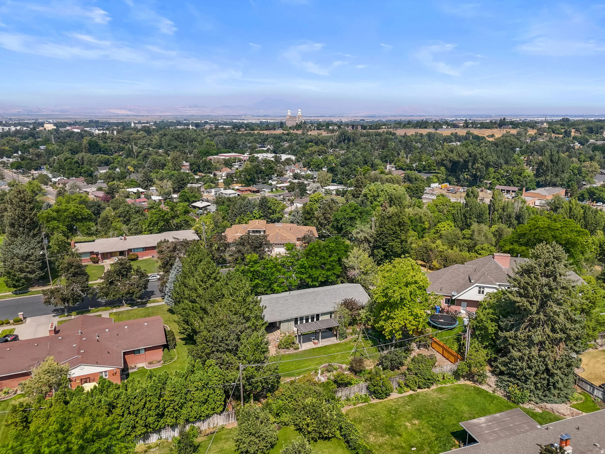 Aerial perspective showcasing mature landscaping with established trees throughout the property, expansive manicured lawn, and a residential setting within an established neighborhood