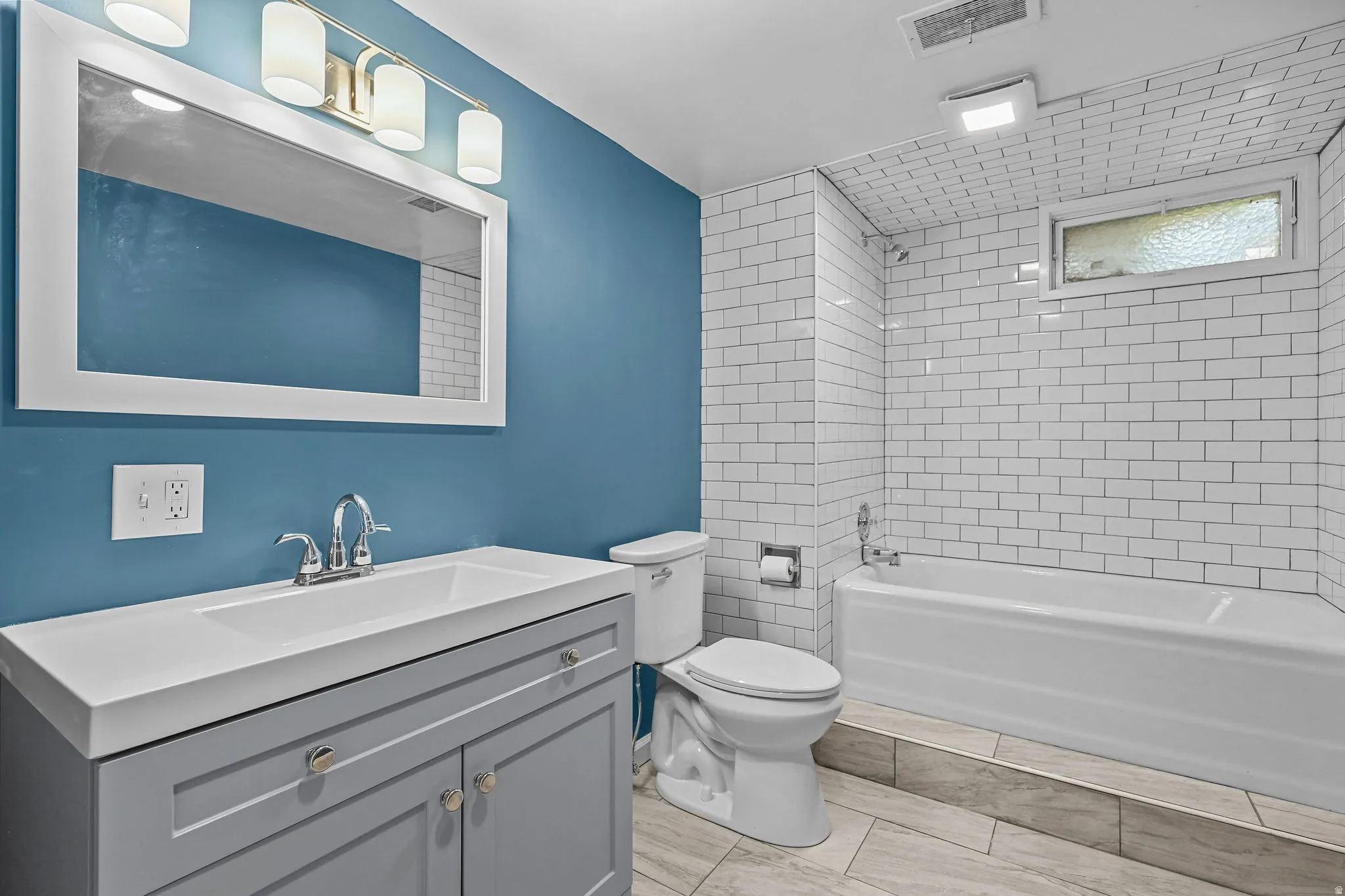 Modern bathroom featuring a striking teal accent wall, white subway tile surround, and a gray vanity with a white quartz countertop and chrome faucet