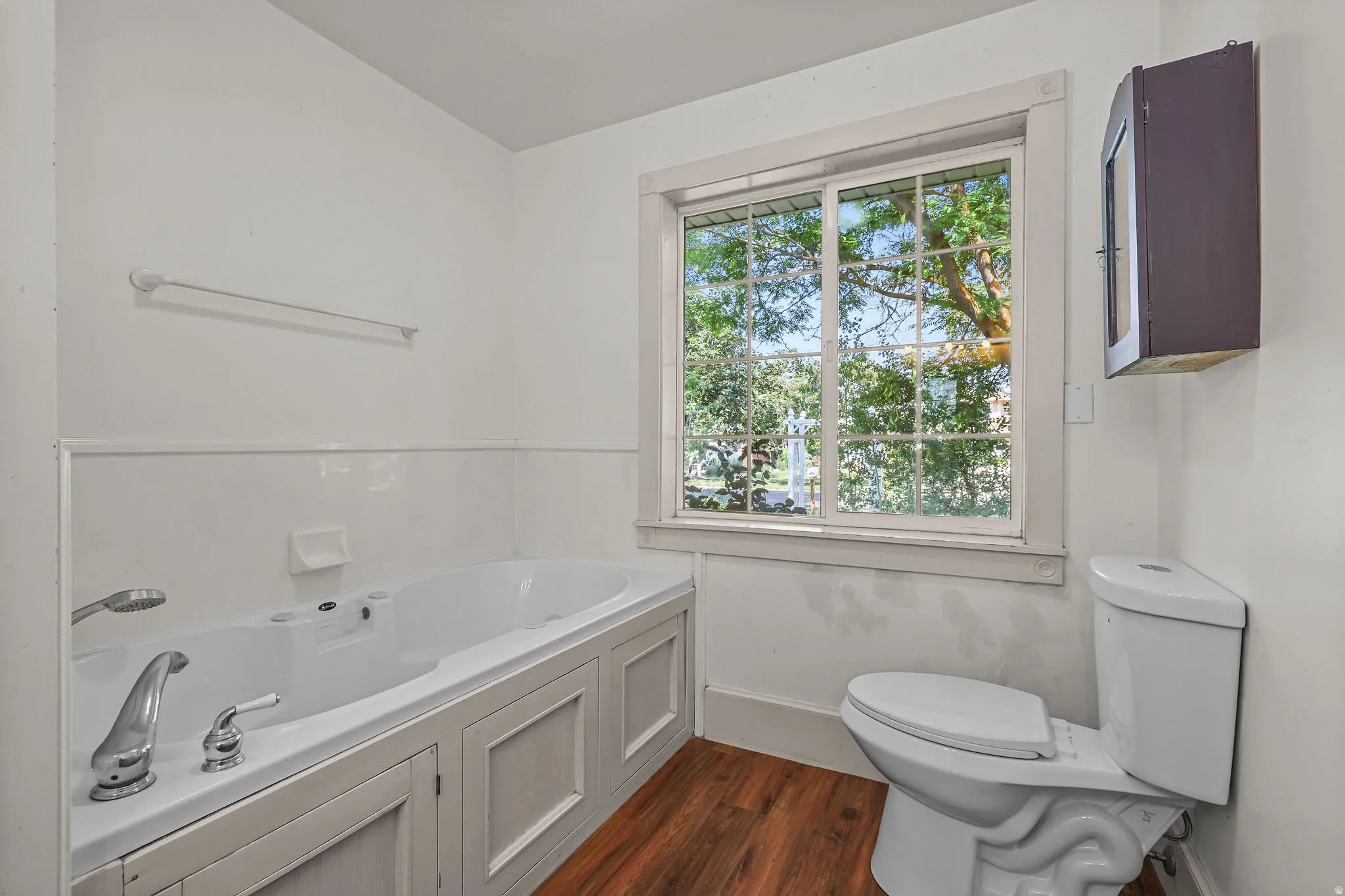 Built-in soaking tub with paneling, wood-finish flooring, and a large window with grilles